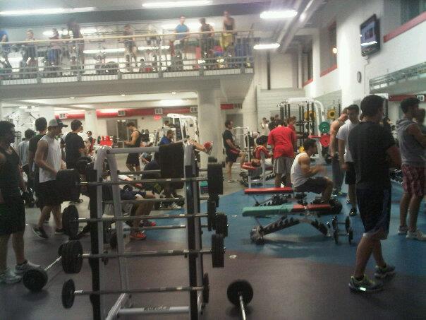 Crowded commercial gym interior with numerous people training, showcasing various equipment and workout stations, illustrating the busy environment typical of peak hours.